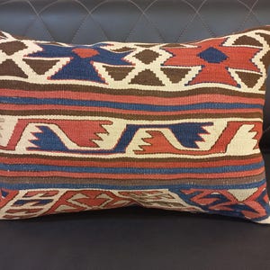 May include: A rectangular pillow with a colorful geometric pattern in shades of red, blue, brown, and white. The pillow is made of woven fabric and has a traditional design.