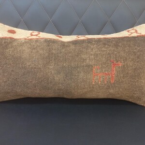 May include: A brown and beige throw pillow with a red embroidered design of a stylized animal. The pillow has a fringe border.