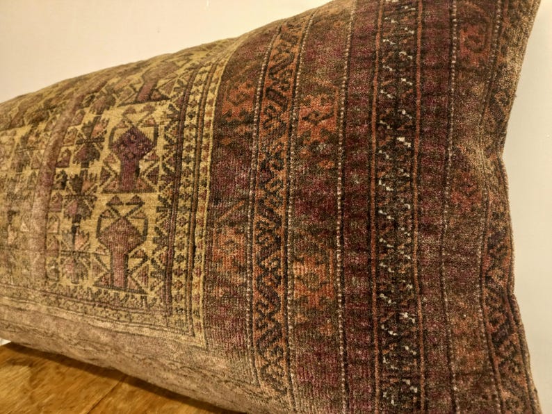 May include: A rectangular decorative pillow with a vintage, patterned design. The pillow features a mix of colors, including brown, beige, and burgundy. The design includes geometric shapes and vertical stripes, creating a textured appearance. The pillow is likely made of a soft fabric.