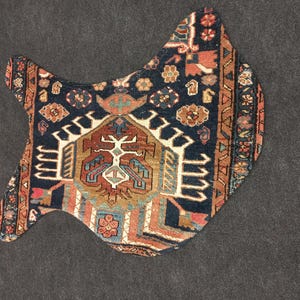May include: A decorative, uniquely shaped rug with a dark blue background and intricate patterns in shades of red, orange, and cream. The rug features a central design with geometric and floral motifs, and a detailed border.