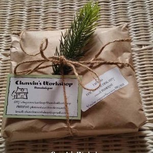 Op de afbeelding: Een pakket verpakt in bruin papier, vastgebonden met touw en versierd met een takje groen. Twee labels zijn bevestigd, een met de tekst "Chawin's Workshop" en de andere met een bedankbericht. Het pakket ligt op een geweven oppervlak.