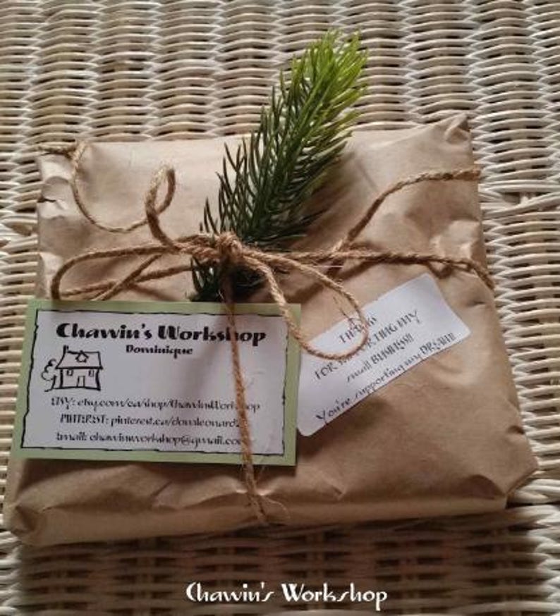 Op de afbeelding: Een pakket verpakt in bruin papier, vastgebonden met touw en versierd met een takje groen. Twee labels zijn bevestigd, een met de tekst "Chawin's Workshop" en de andere met een bedankbericht. Het pakket ligt op een geweven oppervlak.