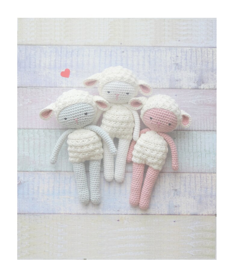 Op de afbeelding: Drie handgemaakte gehaakte schaapjes in wit, lichtblauw en roze. Elke pop heeft een witte body, een bijpassend hoofd en roze accenten op de oren en het gezicht. De poppen zijn gerangschikt op een lichtgekleurd, veelkleurig houten oppervlak.