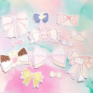 May include: A set of 11 pastel-coloured bow stickers with various designs, including a bunny, a cat, sprinkles, and a rainbow. The stickers are perfect for adding a touch of whimsy to your planner, journal, or scrapbook.