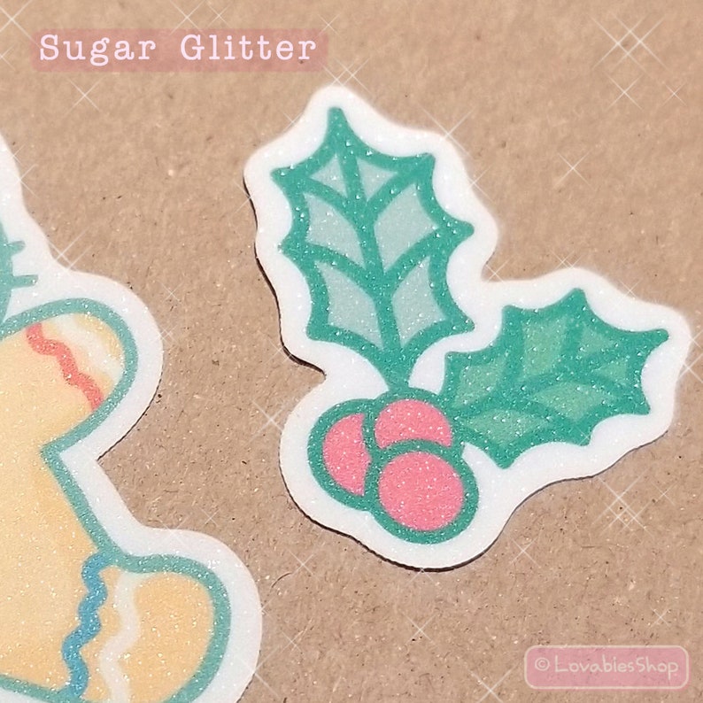 May include: A white sticker with a green holly leaf design and red berries. The sticker has a glittery finish and says "Sugar Glitter" at the top.