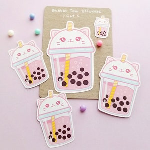 Puede incluir: Cuatro pegatinas de t&eacute; de burbujas rosas y blancas con una cara de gato en la tapa. El texto "Bubble Tea Stickers >Cat<" est&aacute; sobre un fondo marr&oacute;n.