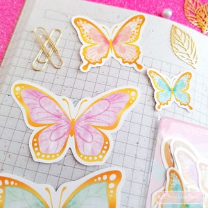 May include: A sheet of colorful butterfly stickers with a watercolor effect. The butterflies are outlined in gold and have pink, blue, and green wings.