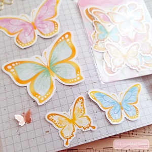 May include: A sheet of colorful butterfly stickers with a watercolor effect. The butterflies are in shades of pink, yellow, blue, and green. The stickers are perfect for adding a touch of whimsy to journals, planners, and other craft projects.