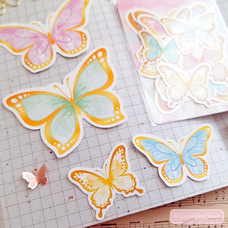 May include: A sheet of colorful butterfly stickers with a watercolor effect. The butterflies are in shades of pink, yellow, blue, and green. The stickers are perfect for adding a touch of whimsy to journals, planners, and other craft projects.