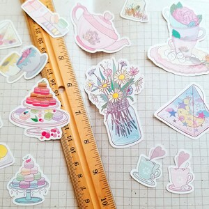 May include: A collection of pastel-colored stickers featuring a variety of designs, including a teapot, flowers in a jar, a cake, a crescent moon, and teacups. The stickers are on a gridded background.