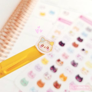 Op de afbeelding: Een vel stickers met schattige cartoon dierengezichten. De stickers zijn op een witte achtergrond en bevatten een verscheidenheid aan dieren, waaronder katten, honden en beren. De stickers zijn perfect om een ​​toets van whimsy toe te voegen aan je planner, dagboek of laptop.