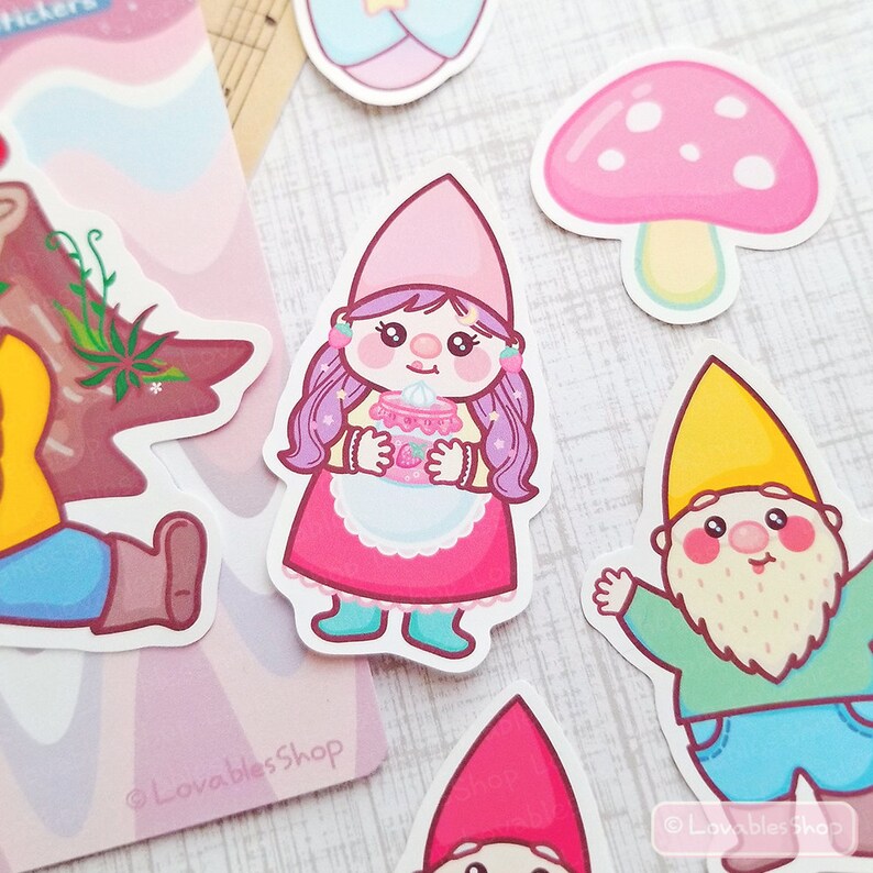 May include: A set of colorful cartoon gnome stickers featuring a pink gnome holding a pink cup with a strawberry, a yellow gnome with a beard, and a pink mushroom with white dots. The stickers are on a white background with a pink and white swirl pattern.