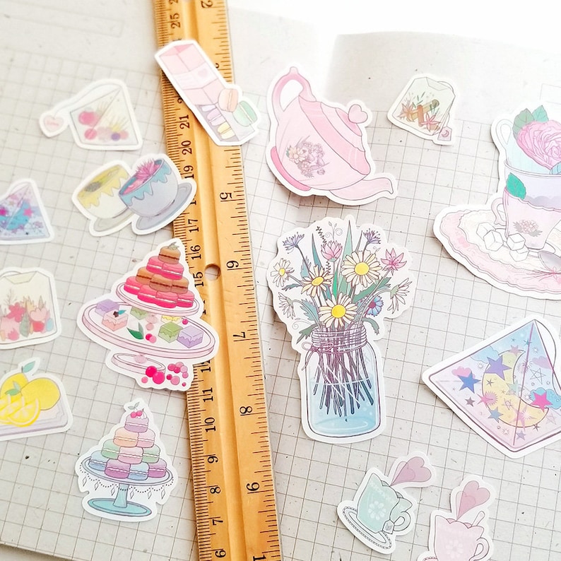 May include: A collection of pastel-colored stickers featuring a teapot, teacups, flowers, pastries, and other whimsical designs. The stickers are arranged on a gridded background.