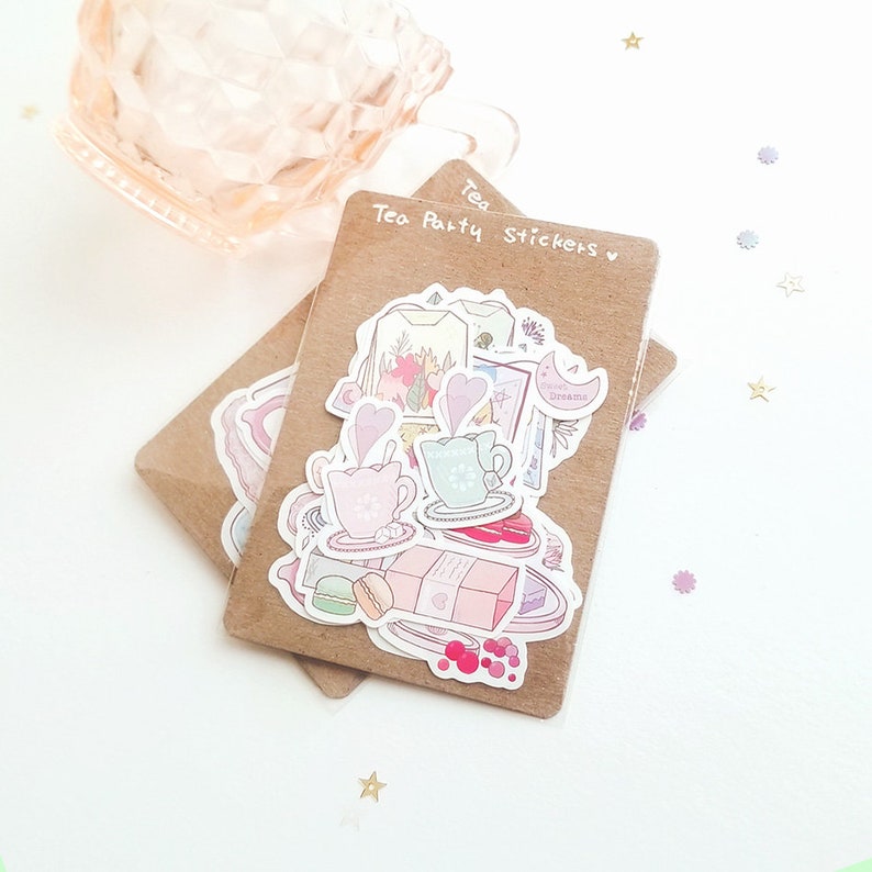 May include: A sheet of stickers featuring a tea party theme. The stickers are on a brown background and include images of teacups, teapots, macarons, and other tea party treats. The text "Tea Party Stickers" is written on the sheet.