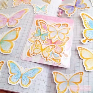 May include: A sheet of butterfly stickers with a watercolor design. The butterflies are in various shades of blue, pink, and yellow with gold accents. The sheet is labeled "Butterfly Stickers".