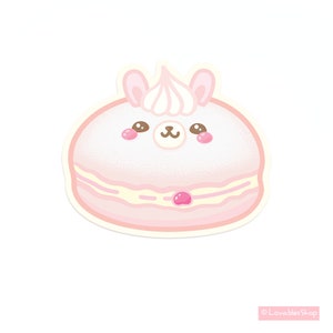May include: A pink and white macaron with a cute cartoon llama face and a pink cherry on top. The macaron is decorated with white sprinkles.