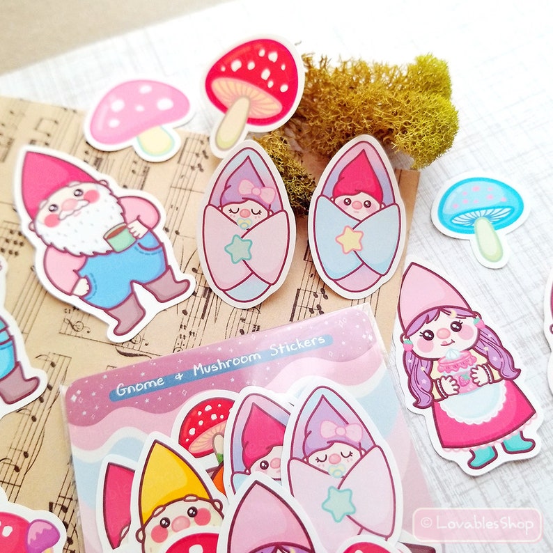 May include: A sheet of stickers featuring gnomes and mushrooms. The stickers are colorful and feature a variety of designs, including gnomes wearing hats and holding mugs, mushrooms with pink and blue tops, and baby gnomes wrapped in blankets. The sheet also includes the text "Gnome + Mushroom Stickers".