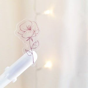 May include: A clear sticker with a pink outline of a single flower with leaves.