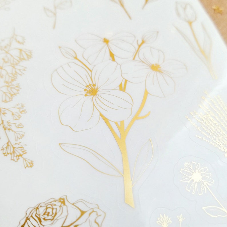 May include: Gold foil stickers featuring a variety of floral designs, including a cluster of delicate flowers with a long stem, a single rose, and a small daisy.