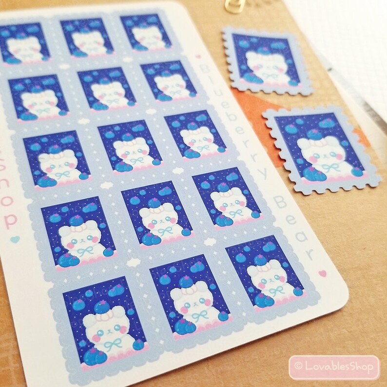May include: A sheet of 12 stickers featuring a white bear holding a basket of blueberries. The stickers are in the shape of a postage stamp with a blue background and white stars. The text "Blueberry Bear" is printed on the sheet.