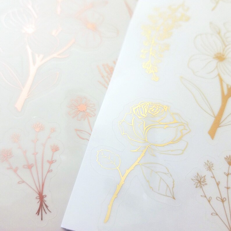 May include: Two sheets of clear sticker paper with gold and rose gold floral designs. The designs include a rose, leaves, and various small flowers.