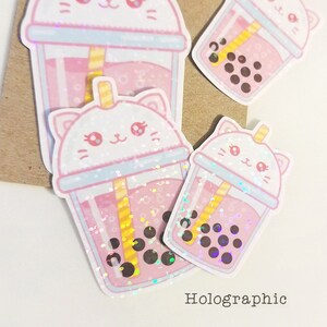 Puede incluir: Tres pegatinas hologr&aacute;ficas de t&eacute; de burbujas rosa con una linda carita de gato en la tapa. Las pegatinas est&aacute;n sobre un fondo de papel marr&oacute;n. Hologr&aacute;fico.