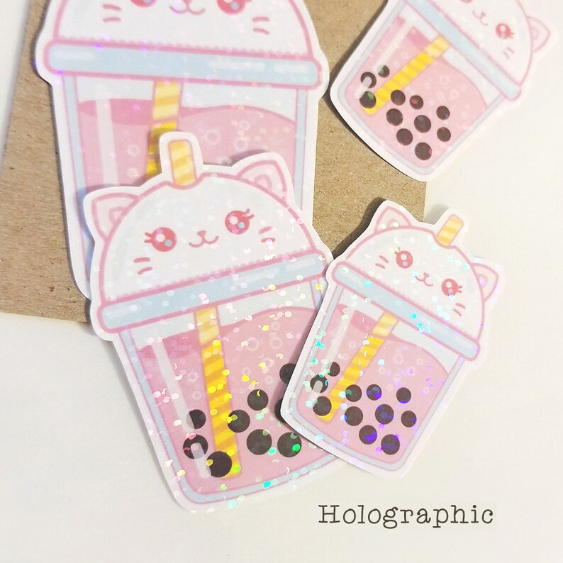 Puede incluir: Tres pegatinas hologr&aacute;ficas de t&eacute; de burbujas rosa con una linda carita de gato en la tapa. Las pegatinas est&aacute;n sobre un fondo de papel marr&oacute;n. Hologr&aacute;fico.