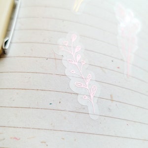 May include: A clear sticker with a pink floral design. The sticker features a delicate branch with small leaves and flowers.