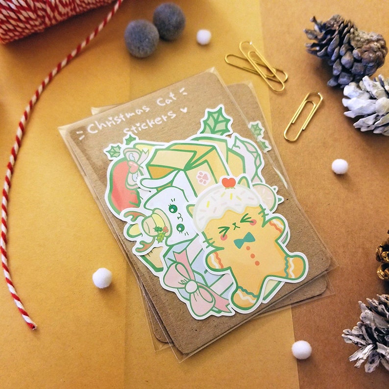 May include: A set of Christmas cat stickers featuring a gingerbread cat, a cat wearing a Santa hat, and a cat in a box. The stickers are on a brown background with the text "Christmas Cat Stickers" written in white.