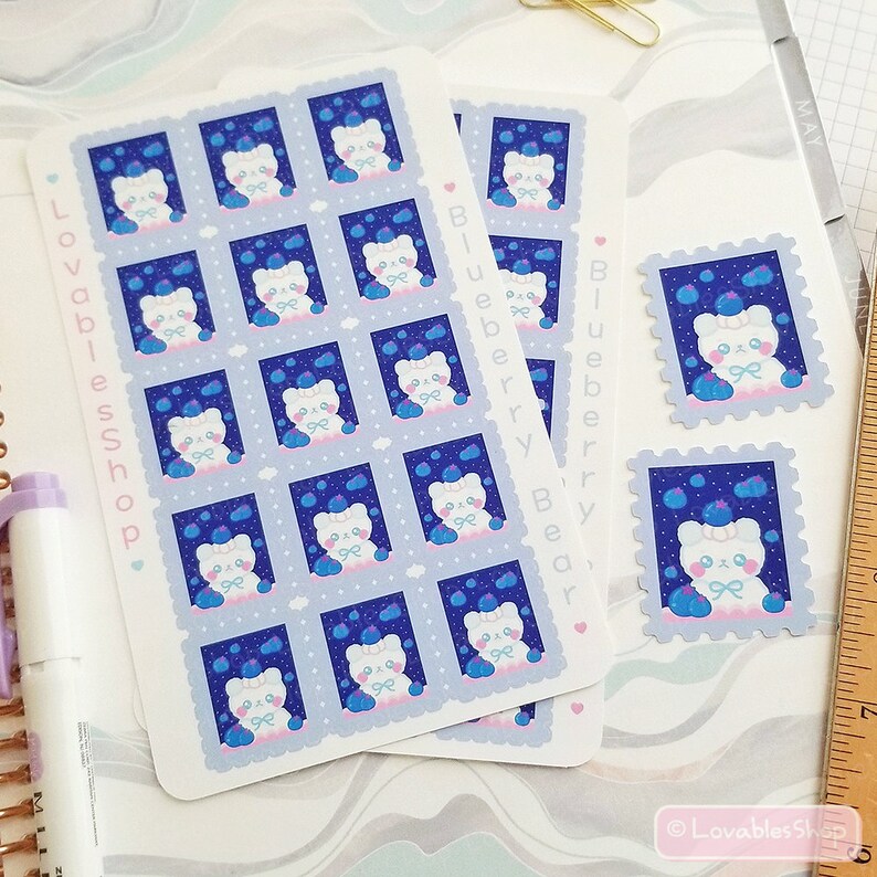 May include: A sheet of stickers featuring a cartoon bear wearing a blue hat and holding blueberries. The stickers are on a blue background with white clouds. The text "Blueberry Bear" is printed on the sheet.