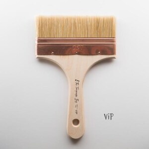 May include: A natural-bristle paint brush with a light wood handle and a copper-colored metal band. The brush head is rectangular, with the bristles extending outwards. The handle has a hole for hanging and the text "The Tempera Iris = VIP".