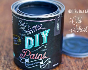 May include: A black metal paint can labeled Debi's Design Diary DIY Paint. The label features white and teal text with the words DIY Paint and Old School. The can is open with a dark grey lid resting nearby on a wooden surface.