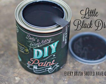 May include: An open metal can of black paint with a matching lid beside it. The label features the text Debi's design diary DIY Paint, Little Black Dress, and Every Brush Should Have One, with decorative white and teal graphic elements.