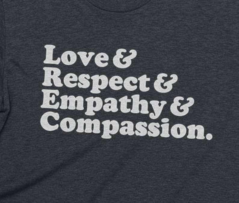 May include: A dark heather grey t-shirt with white text that reads "Love & Respect & Empathy & Compassion."