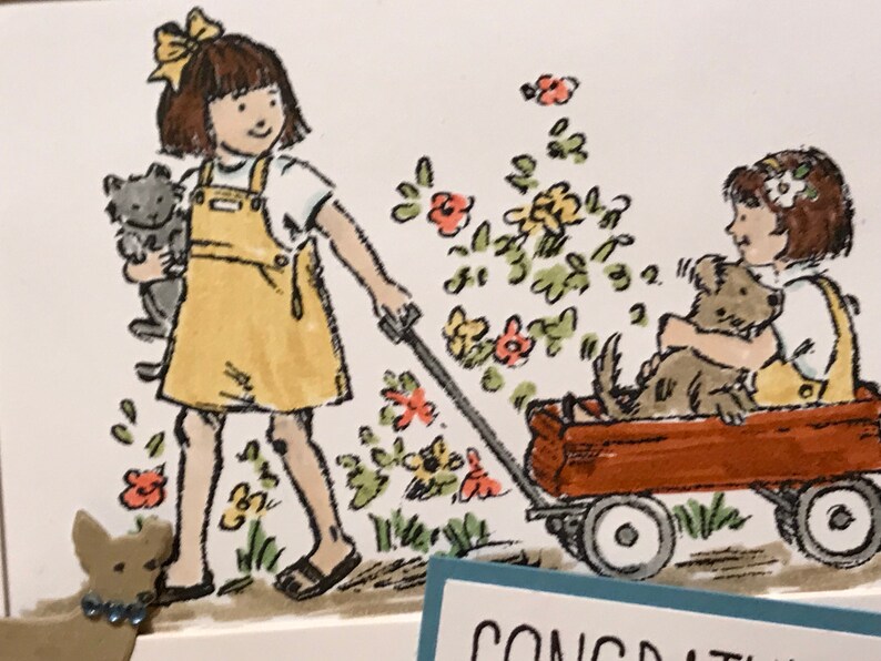 May include: A greeting card illustration featuring two children in yellow overalls, one pulling a red wagon with a dog inside while holding a cat, surrounded by colorful flowers. The text CONGRATULATIONS is partially visible at the bottom edge.