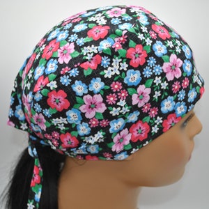 May include: A black fabric headband with a floral print featuring pink, blue, and green flowers. The headband has a long tie that can be tied at the back of the head.