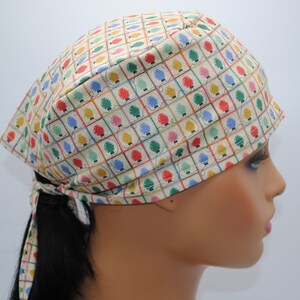 May include: A beige surgical scrub hat with a colorful pattern of small trees in squares. The hat has a tie at the back.