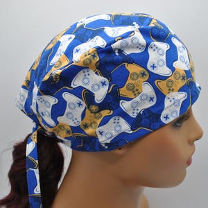 May include: Blue surgical scrub hat with a pattern of white and yellow video game controllers.