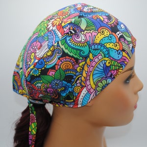 May include: A colorful patterned surgical cap with a tie at the back. The cap features a black background with a variety of bright colors, including blue, green, yellow, pink, and purple. The pattern is made up of swirls, flowers, and other abstract shapes.
