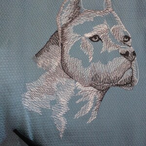 May include: Embroidered image of a white dog's head on a blue fabric background.