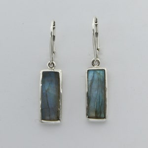 May include: A pair of silver dangle earrings with rectangular labradorite stones. The stones have a blue and green iridescent sheen.