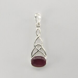 May include: A silver pendant with a Celtic knot design and a deep red oval gemstone. The pendant has a loop at the top for a chain. The gemstone is set in a silver bezel.
