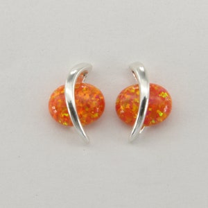 May include: A pair of silver earrings with orange opal stones. The earrings have a curved design and are set with round, sparkly stones.