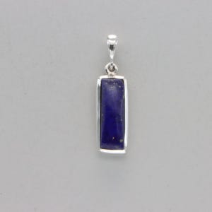 May include: A silver pendant with a rectangular lapis lazuli stone. The stone is a deep blue color with white veins.