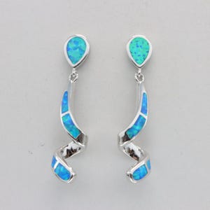 May include: A pair of silver-toned drop earrings featuring a teardrop-shaped top and a spiraling, ribbon-like lower section. Each earring is inlaid with vibrant blue and green iridescent opal-style stones set into the polished metal frame.
