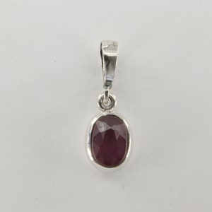 May include: A silver pendant with a red oval gemstone. The pendant has a simple design and is perfect for adding a touch of elegance to any outfit.