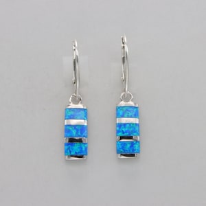 Puede incluir: Un par de pendientes de plata con detalles de piedra de ópalo azul. Las piedras están engastadas en forma rectangular y tienen un patrón de rayas.