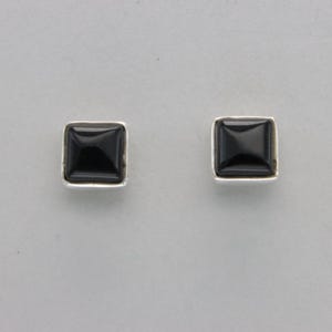 May include: A pair of silver earrings with black square-shaped stones.