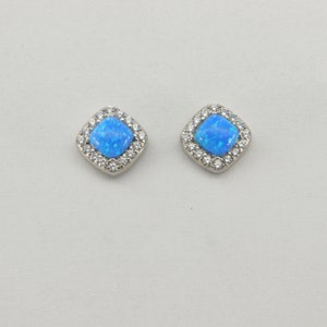 Puede incluir: Un par de pendientes de plata con una piedra de ópalo azul cuadrada engastada en un marco cuadrado de piedras de circonita cúbica transparentes.