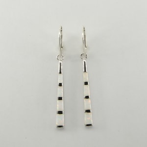 May include: A pair of silver hoop earrings with white and black opal dangle drops. The earrings are made of sterling silver and feature a geometric design.